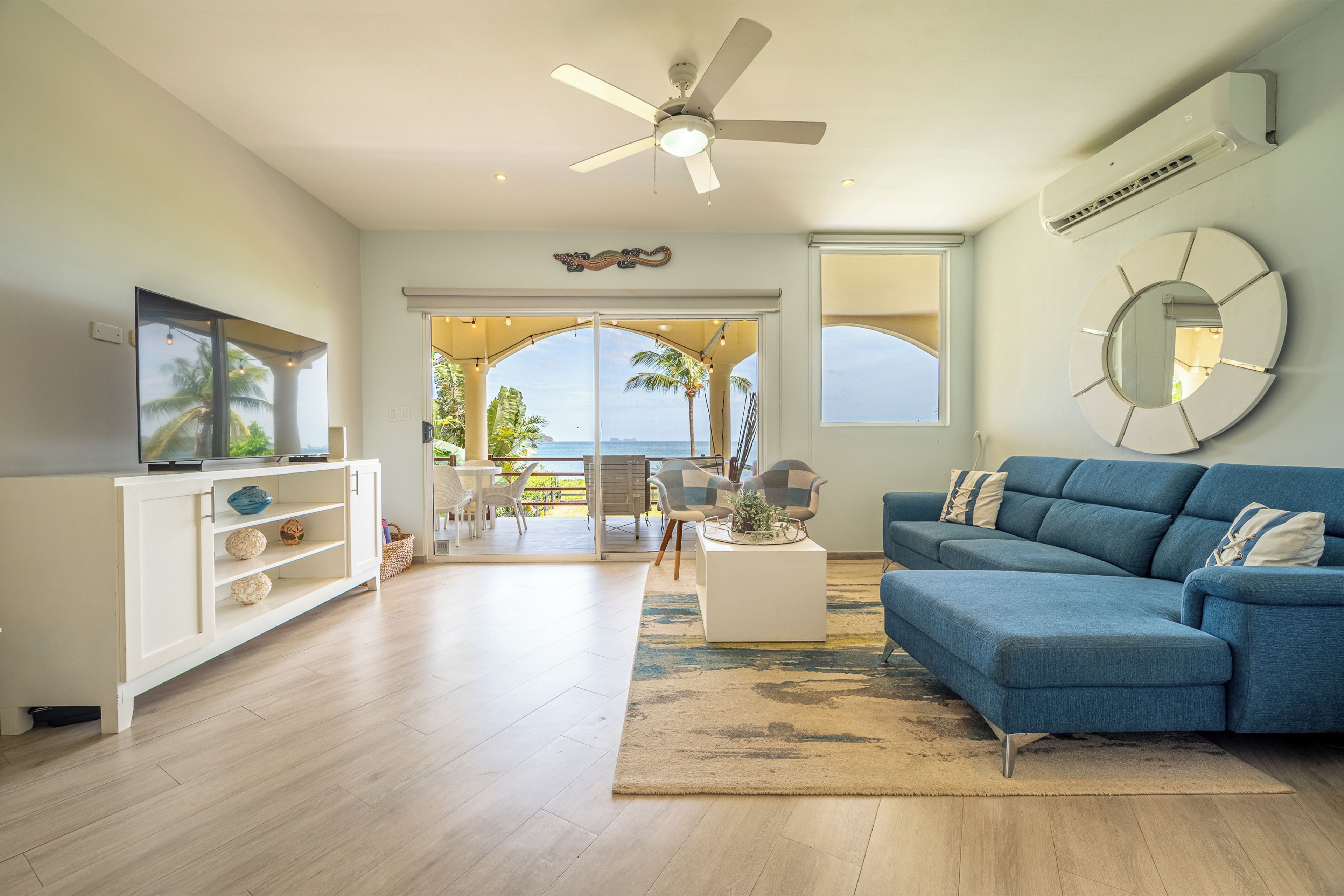 A modern living room with a blue sofa, white entertainment unit, and a ceiling fan.