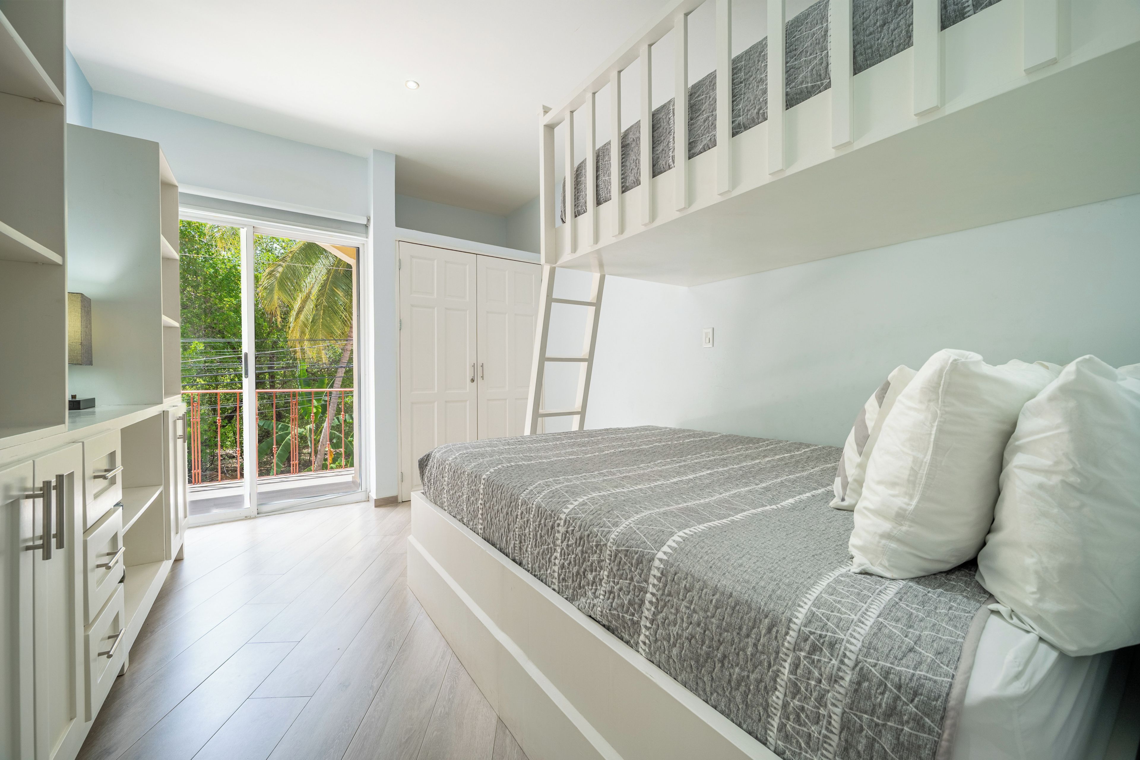 A bedroom with a bunk bed, a wardrobe, and a balcony with a view of greenery.