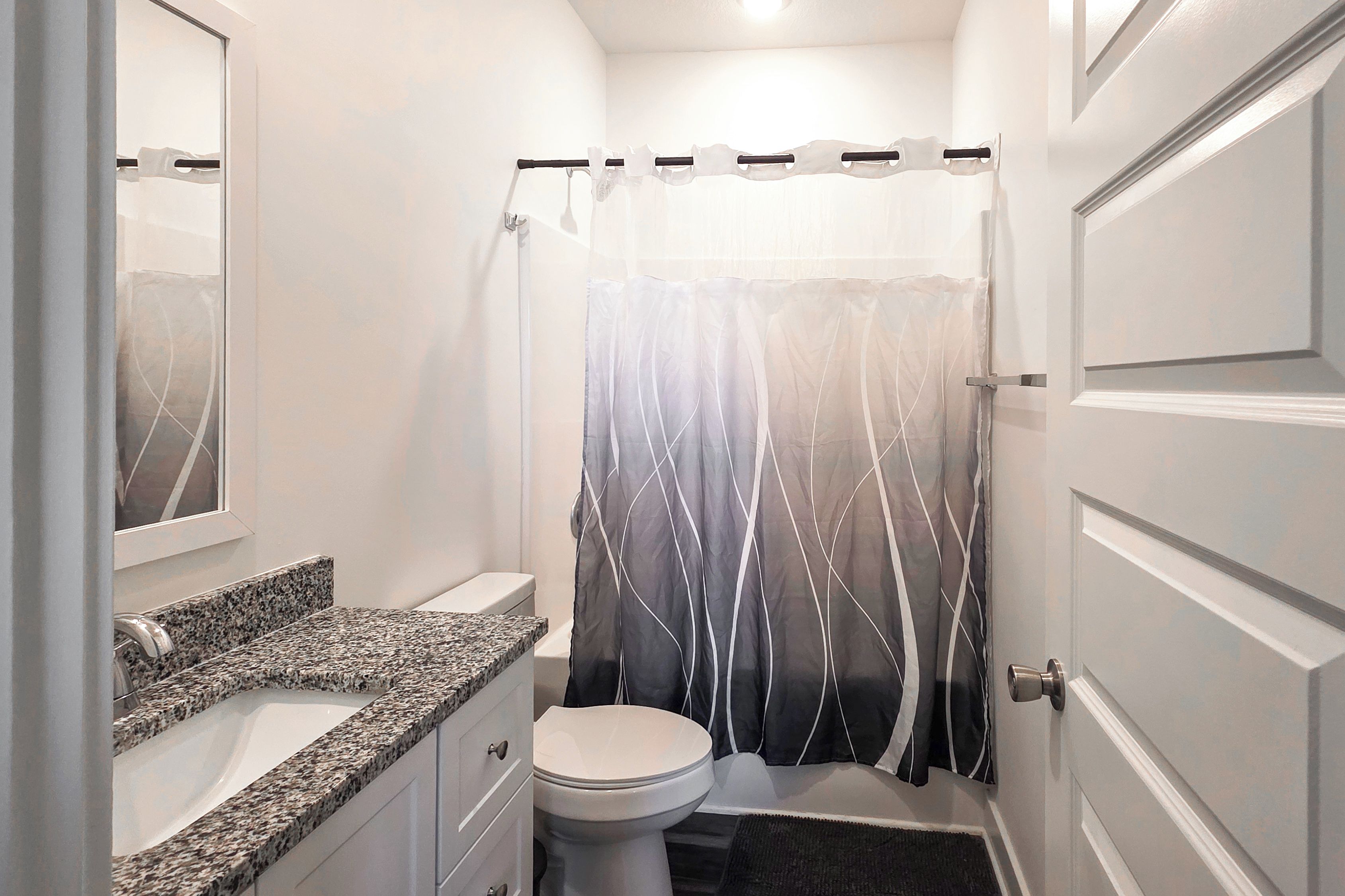 Une salle de bain avec un comptoir en granit, des toilettes et un rideau de douche à motifs ondulés.