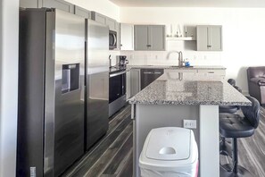 A modern kitchen with stainless steel appliances, a granite countertop, and a built-in dishwasher. - Walk to Parks & Dining! Newly Built Wichita Condo (Wichita)