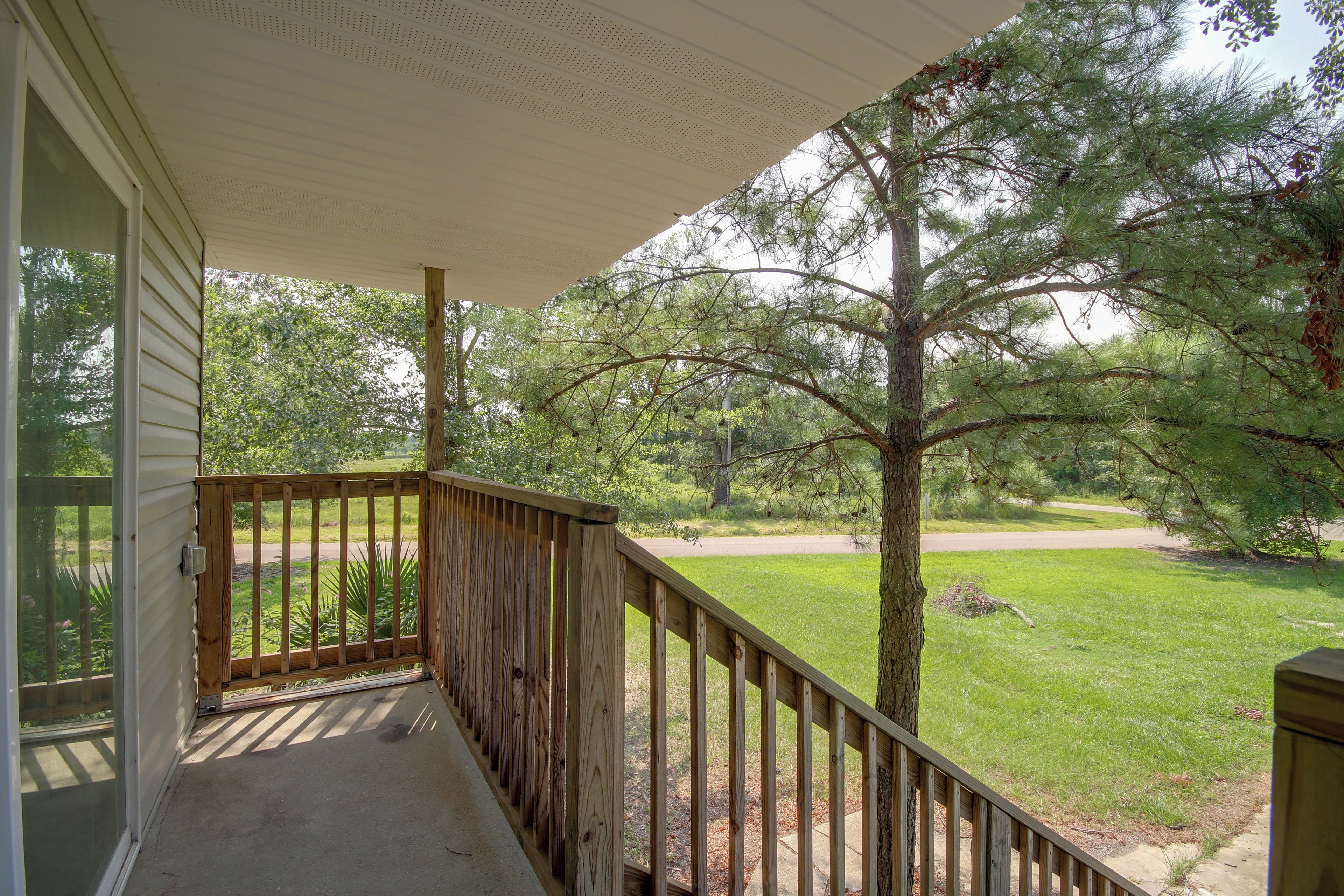 A covered porch with a view of a grassy yard and trees.