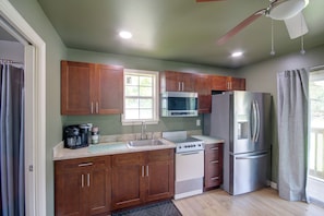 A kitchen with wooden cabinets, a stainless steel refrigerator, a microwave, and a coffee maker. - 4 Mi to Beach! Canal-front Escape in Bay St Louis (Bay St Louis)