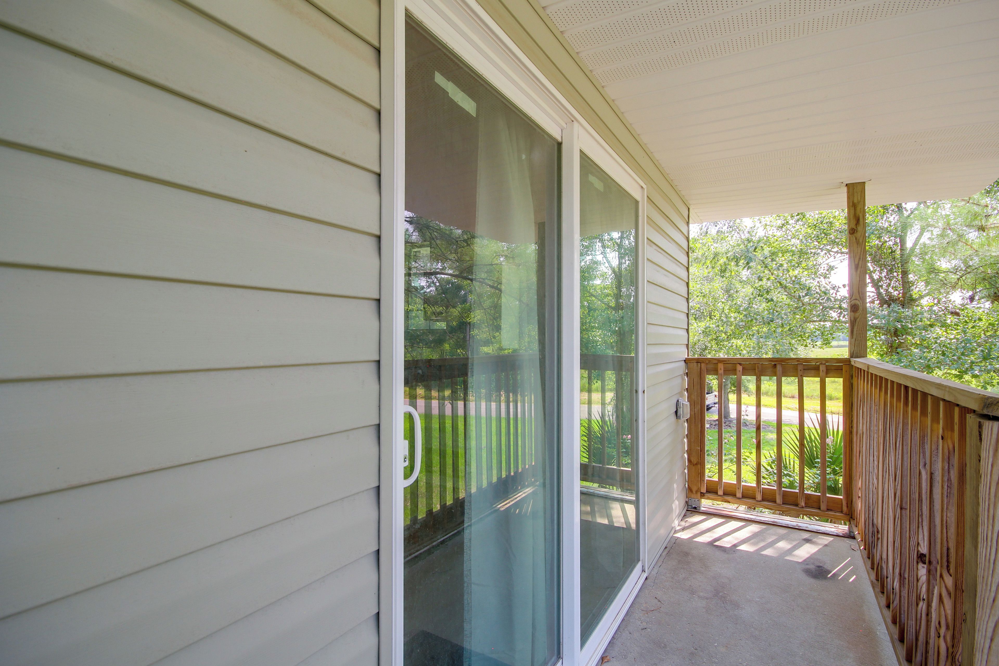 A covered porch with a wooden railing, a sliding glass door, and a view of a green landscape.