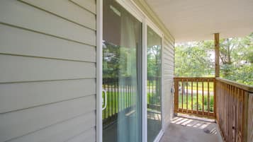 A covered porch with a wooden railing, a sliding glass door, and a view of a green landscape.