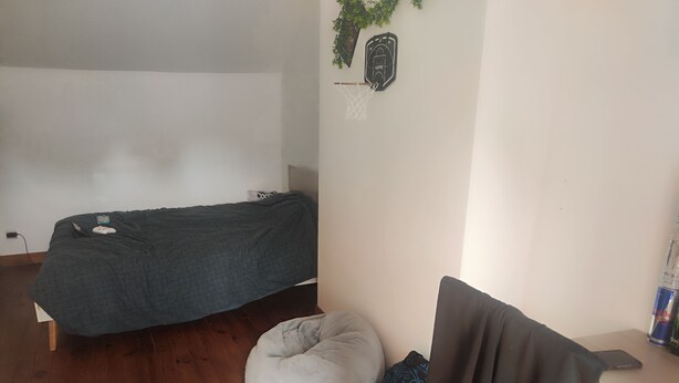 Una habitación con una cama, un sillón de mimbre, una silla y un escritorio con una computadora portátil.