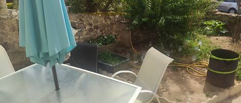 An outdoor seating area with a table and chairs, surrounded by greenery and a stone wall.