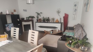 Una sala de estar moderna con comedor, televisor y varios objetos decorativos, entre ellos plantas y obras de arte.
