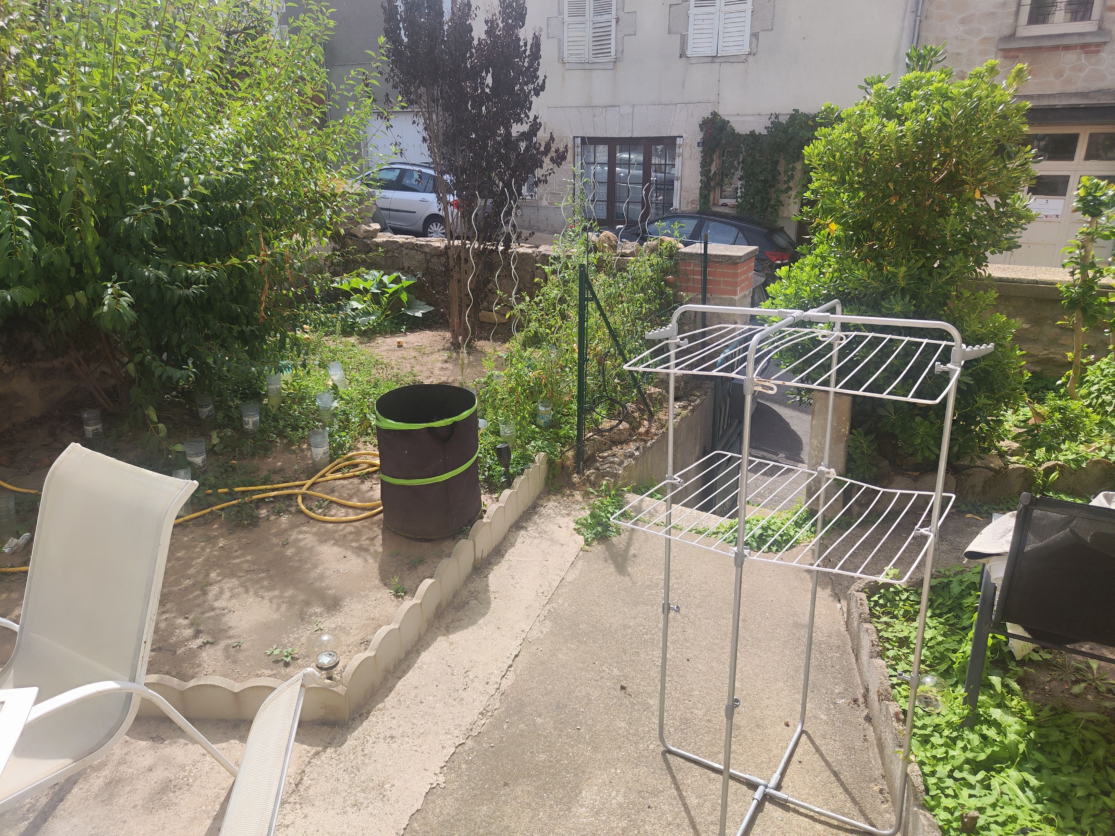 Un jardín con un tendedero de metal, un barril grande y una silla blanca.