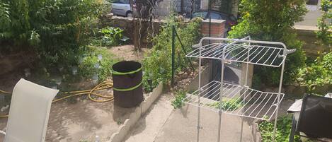 A garden area with a metal drying rack, a large barrel, and a white chair.