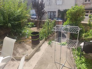 Un jardín con un tendedero de metal, un barril grande y una silla blanca.