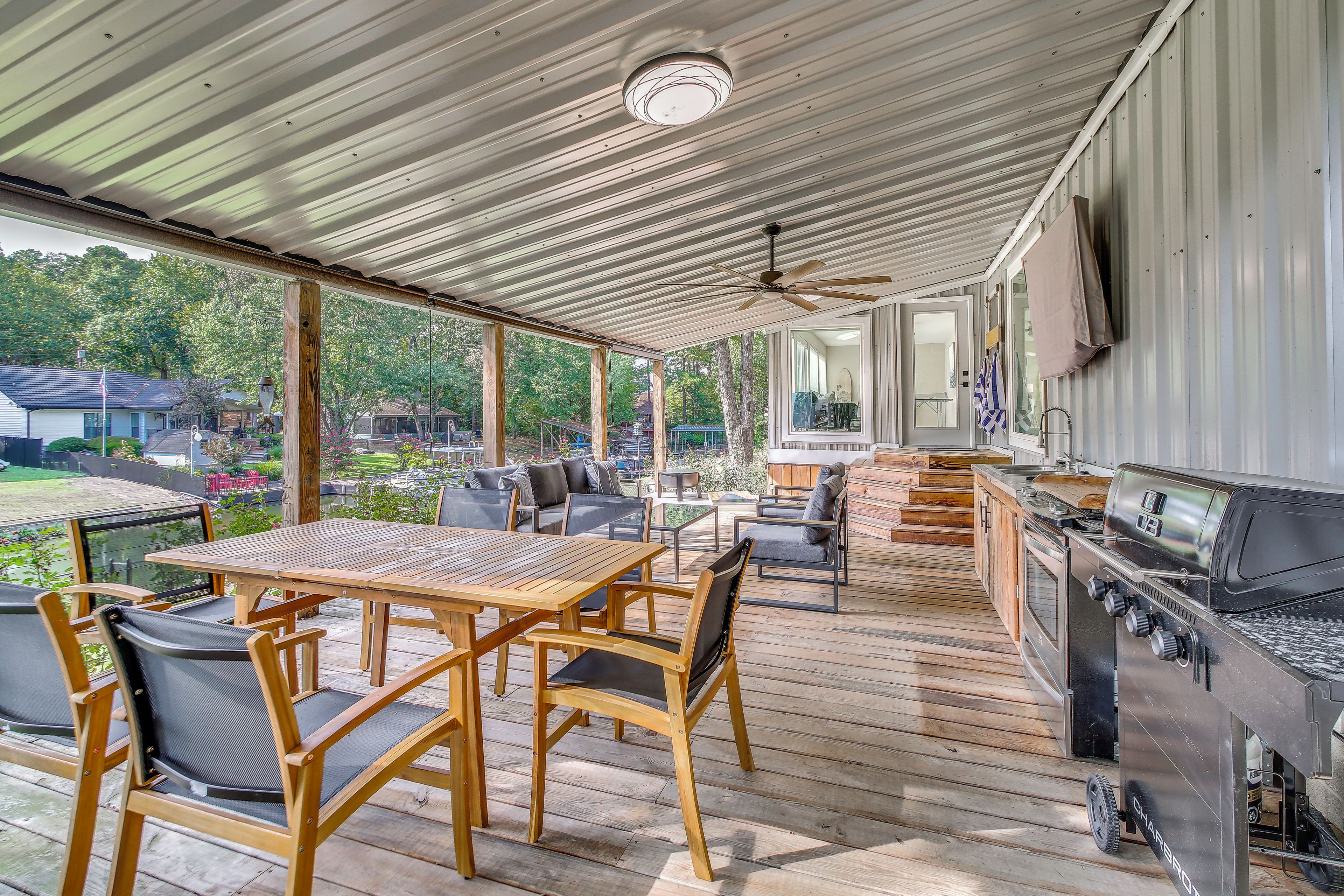 An outdoor patio with a wooden table and chairs, a grill, and a view of the surrounding area.