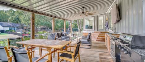 An outdoor patio with a wooden table and chairs, a grill, and a view of the surrounding area.