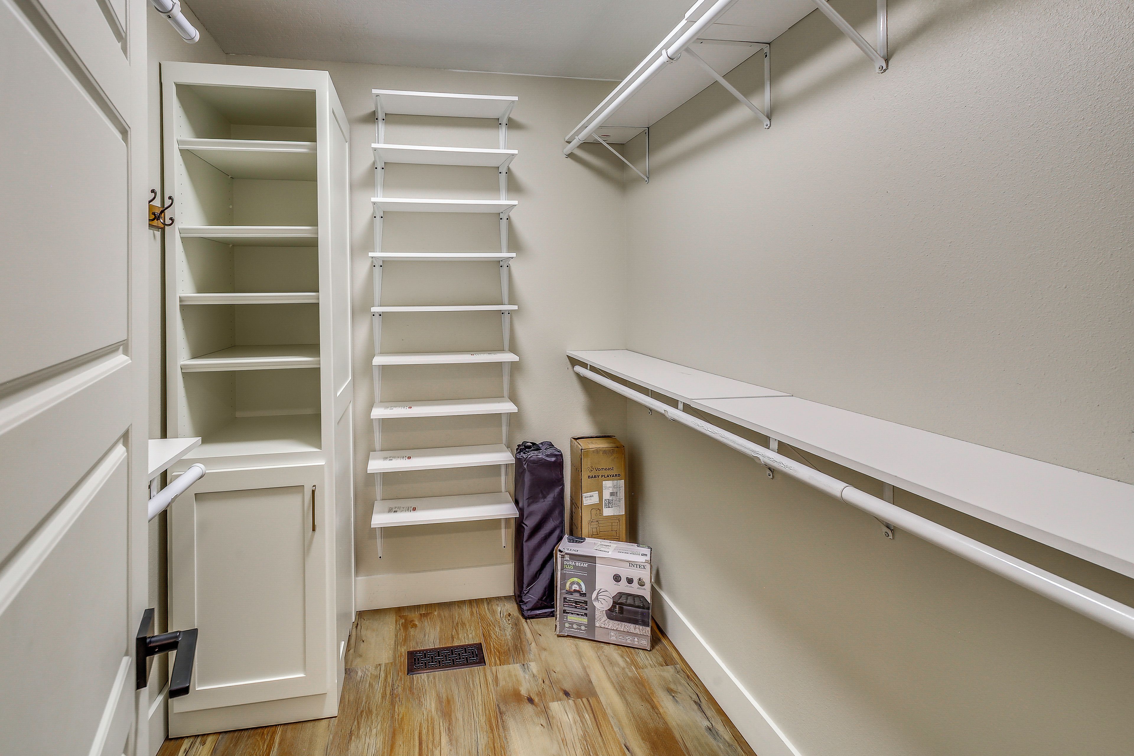 Un dressing accessible sans porte, doté d’étagères ouvertes, d’une porte et d’une grille d’aération au sol.