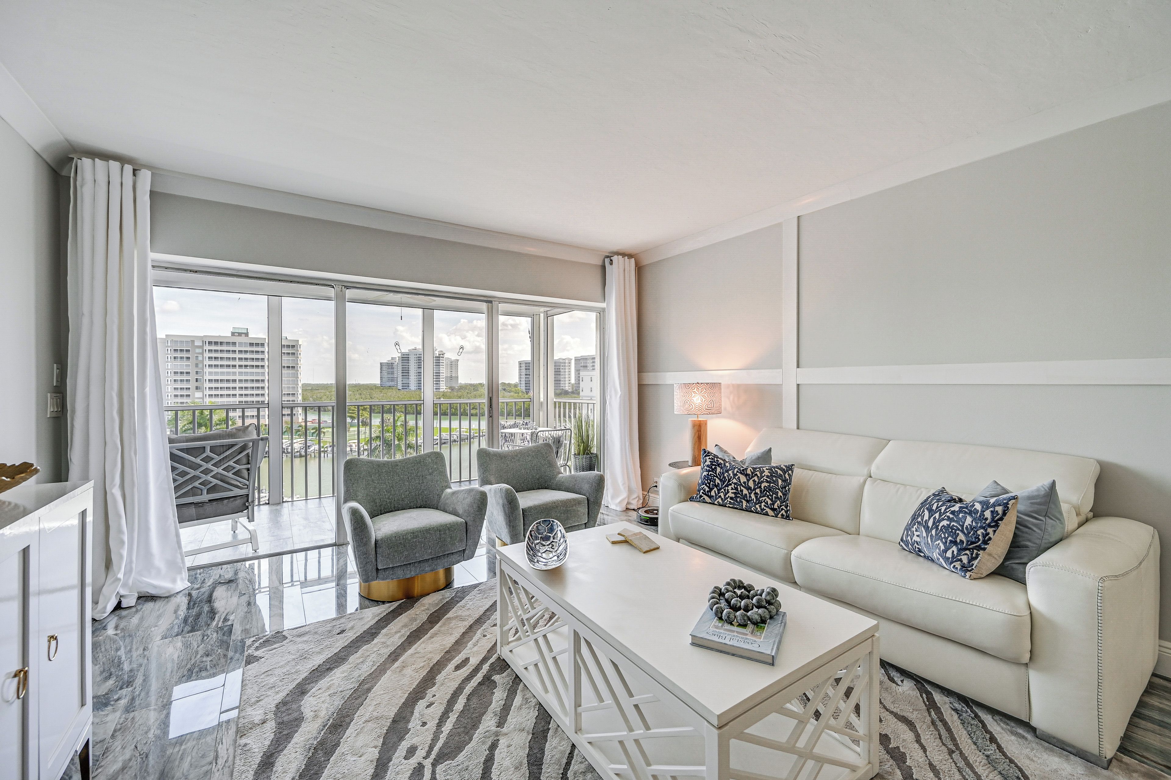 A modern living room with a sofa, armchairs, a coffee table, and a view of high-rise buildings.