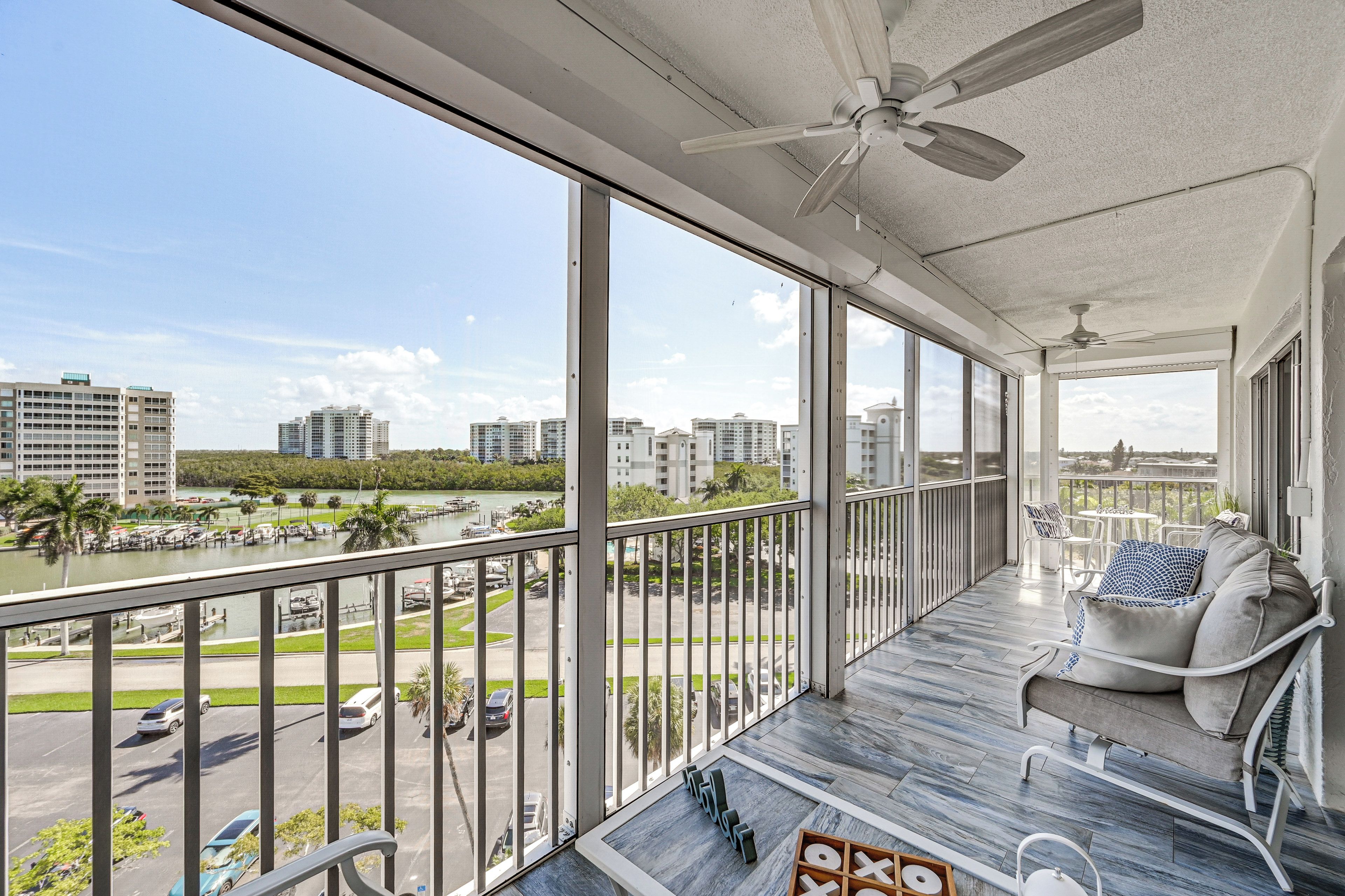 A balcony with a view of a marina and cityscape, furnished with a sofa and chairs.