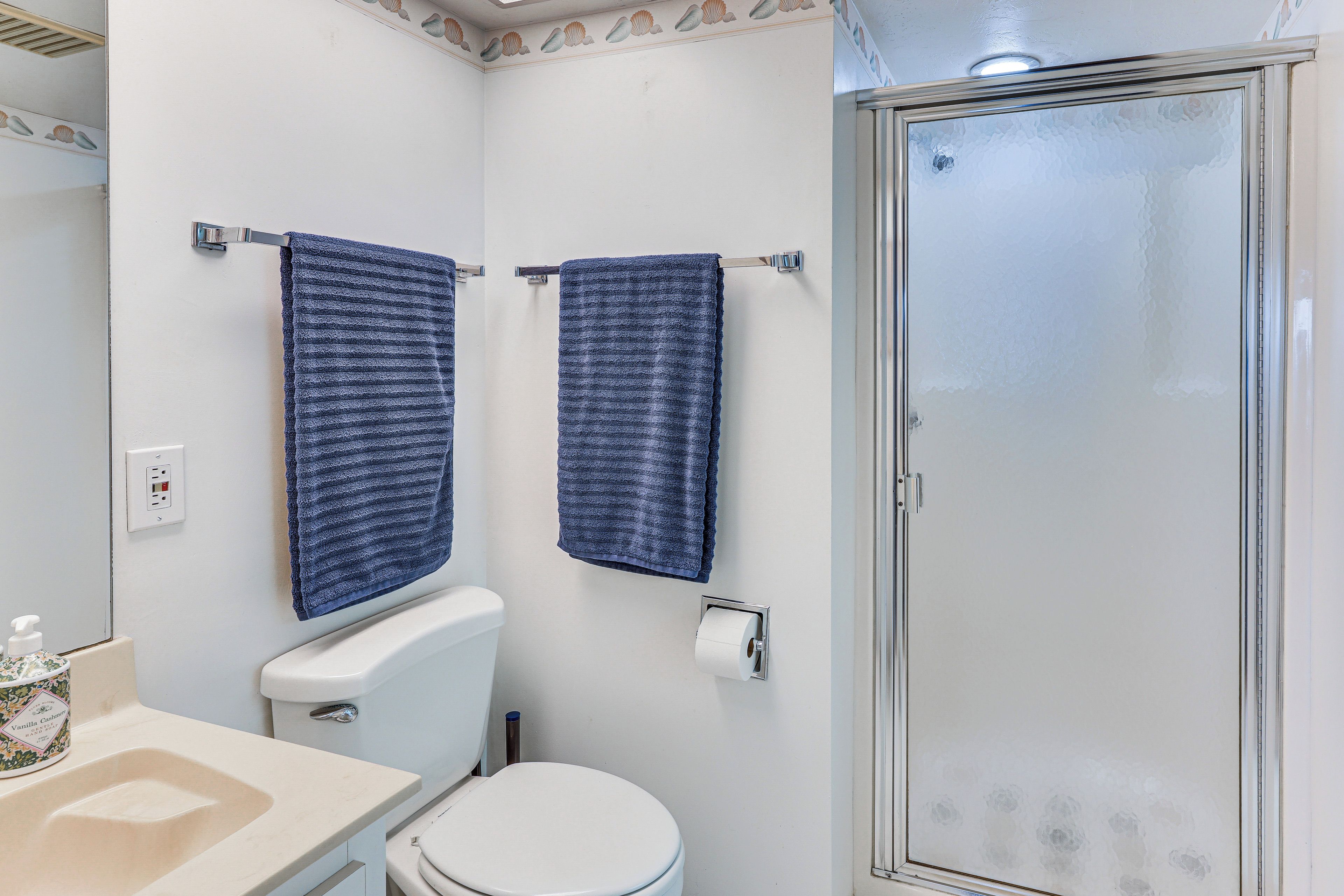 Une salle de bain équipée de toilettes, d’un lavabo et d’une douche. Deux serviettes sont suspendues à des porte-serviettes.