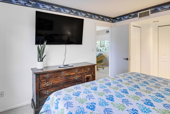 A bedroom with a bed, dresser, TV, and a door leading to another room.