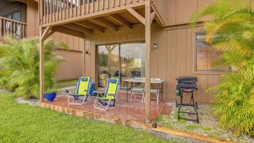 A covered patio area with two lawn chairs, a table, and a barbecue grill.