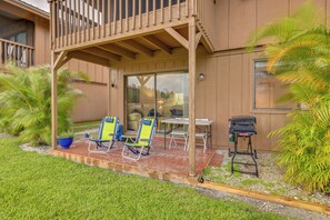 Ein überdachter Patio-Bereich mit zwei Liegestühlen, einem Tisch und einem Grill.