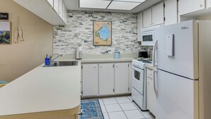 Une cuisine de taille réduite, dotée d’un plan de travail blanc, d’une cuisinière, d’un réfrigérateur et d’un four à micro-ondes.