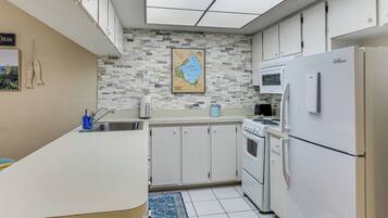 A compact kitchen with a white countertop, a stove, a refrigerator, and a microwave.