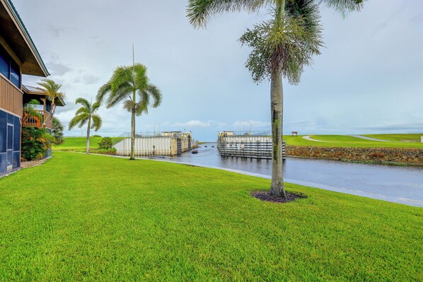 A waterfront property with a grassy lawn, palm trees, and a gated entrance.