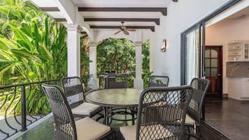 A covered outdoor dining area with wicker furniture, a central table, and a ceiling fan.