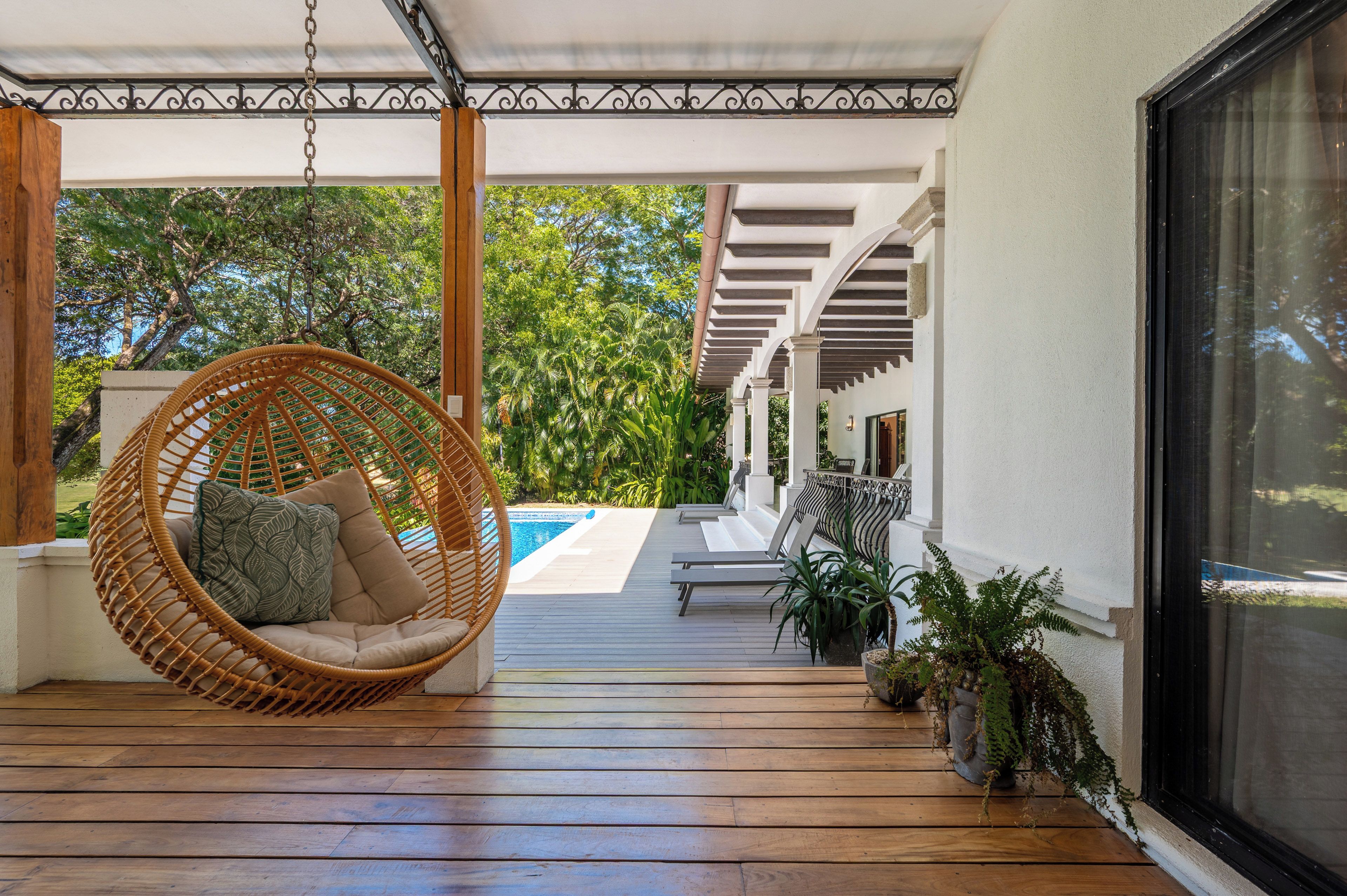 Une terrasse en bois avec un fauteuil suspendu, une piscine et des plantes en pot.