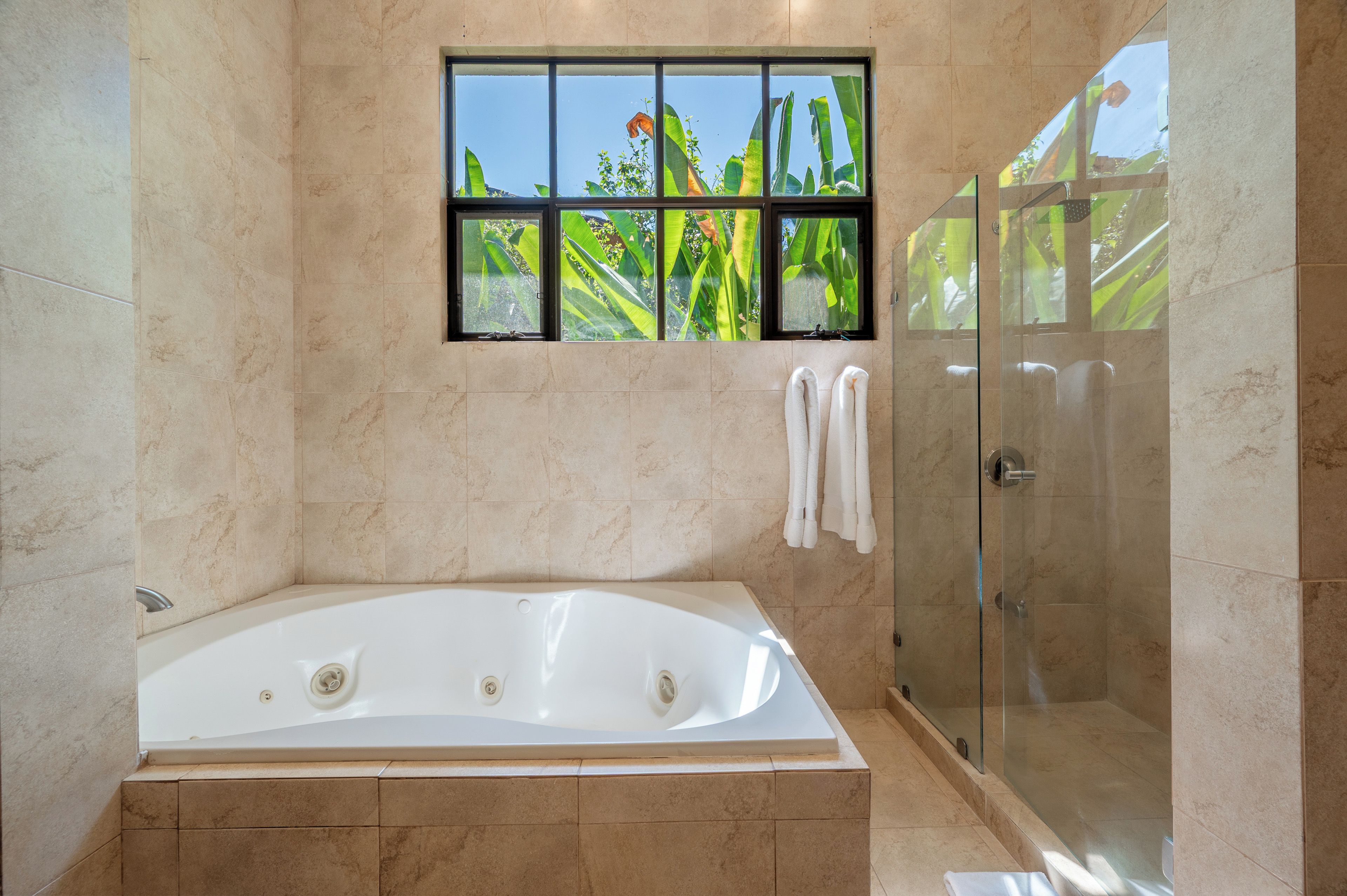 A bathroom with a bathtub, a glass shower enclosure, and a window with a view of greenery.