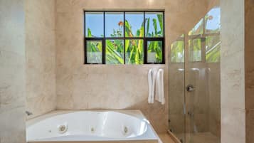 A bathroom with a bathtub, a glass shower enclosure, and a window with a view of greenery.