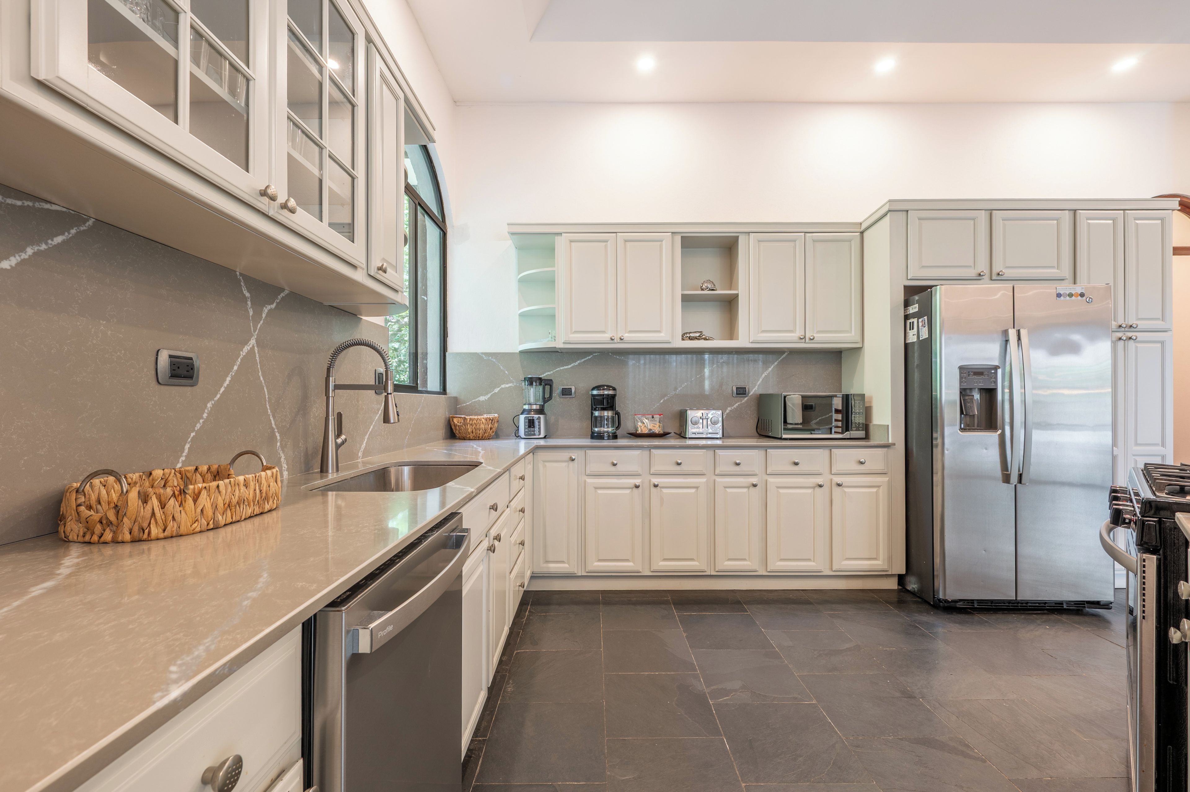 A modern kitchen with stainless steel appliances, a marble countertop, and light-colored cabinetry.