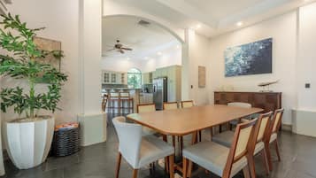 A spacious dining area with a large wooden table and chairs, a ceiling fan, and a view into the kitchen area.