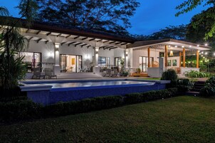 Una casa moderna con piscina, mobiliario exterior y un patio cubierto.