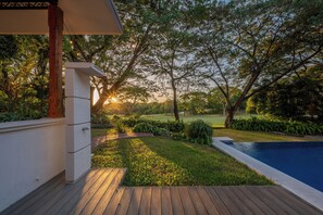A wooden deck with a pool, surrounded by lush greenery and trees.
