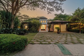 A house with a paved driveway, a covered porch, and a garden with various plants.