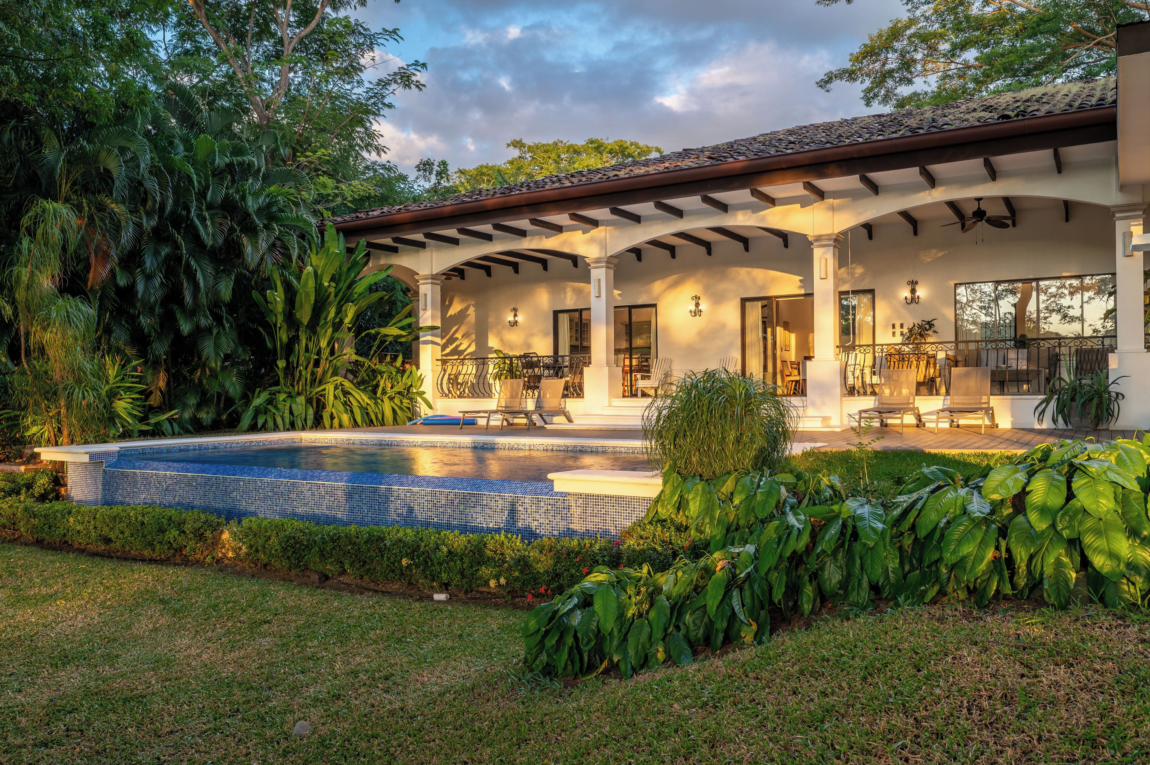 A house with a swimming pool, covered patio, and lush greenery.