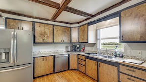 Una cocina moderna con armarios de madera, un refrigerador de acero inoxidable, un lavavajillas y un amplio ventanal con vistas al exterior.