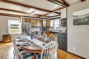 A dining area with a wooden table set for six, surrounded by white chairs with plaid cushions.