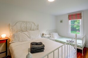 A bedroom with a double bed, a smaller bed, a nightstand with a lamp, and a window with a view of greenery. - Hot Tub, Sauna, Fire Pit! Catskills Family Retreat (Ellenville)