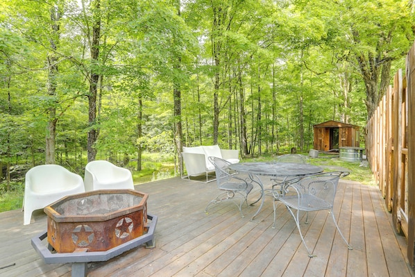 A wooden deck with outdoor furniture, a metal table, and a rustic fire pit.