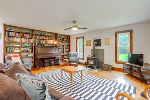 A spacious living room with a large bookshelf, a fireplace, a television, and a piano. - Hot Tub, Sauna, Fire Pit! Catskills Family Retreat (Ellenville)