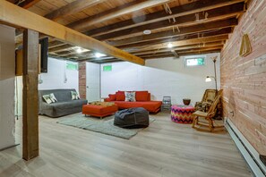 A cozy room with a wooden ceiling, a grey sofa, a red sofa, a wooden rocking chair, and a small table with a lamp. - Hot Tub, Sauna, Fire Pit! Catskills Family Retreat (Ellenville)