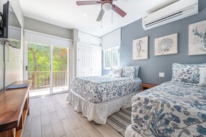 Ein Schlafzimmer mit zwei Betten, einem Deckenventilator, einer Klimaanlage und Blick auf Grünanlagen durch die Schiebetüren.