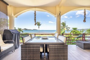 Eine Terrasse im Freien mit einem Tisch aus Glas und Korbmöbeln, mit Blick auf einen Strand und den Ozean.