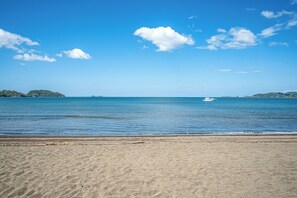 Ein Strand mit klarem, blauem Wasser, ein Boot in der Ferne und ein sandiger Uferstreifen.