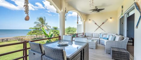 Un espace extérieur aménagé avec des meubles en osier, une table en verre et une vue sur l’océan.