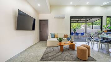 Una sala moderna con televisor de pantalla plana, sofá, mesa de centro y zona de comedor con sillas y mesa.