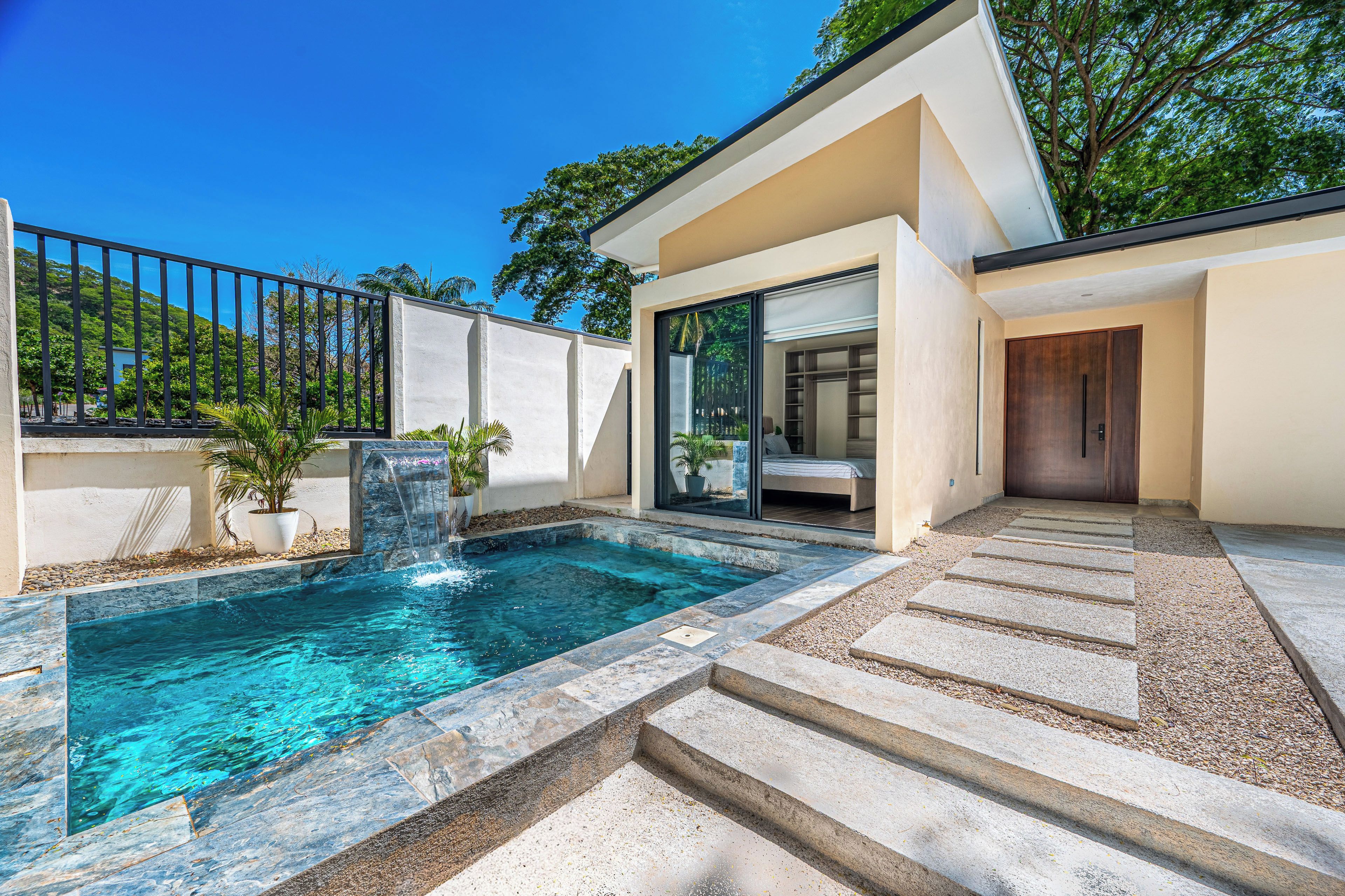Una casa moderna con piscina, un ventanal de vidrio que da a un dormitorio y una escalera de piedra.