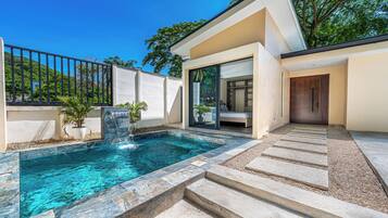 Una casa moderna con piscina, un ventanal de vidrio que da a un dormitorio y una escalera de piedra.