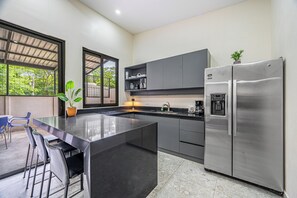 A modern kitchen with a central island, stainless steel appliances, and a view through a large window.